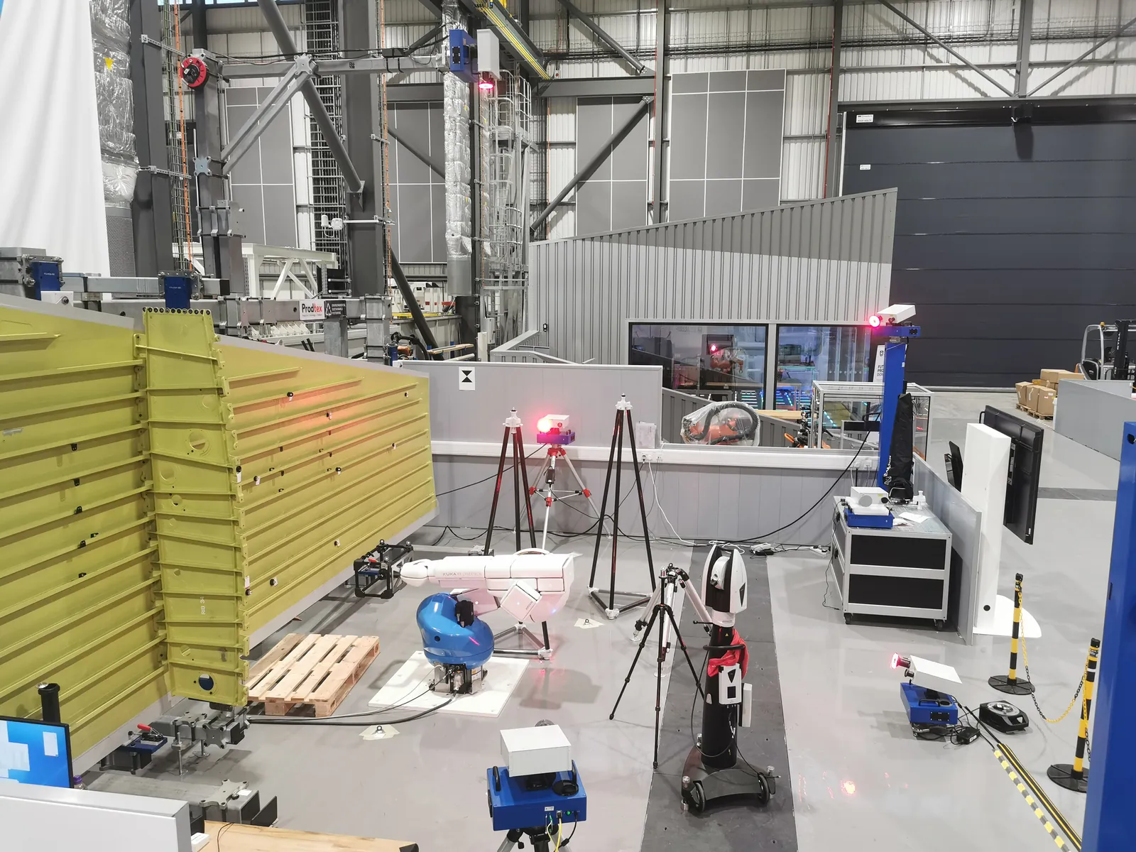 The Metralis development cell at AMRC Cymru: laser trackers on tripods, sensor heads and a robot measuring a large aerospace panel